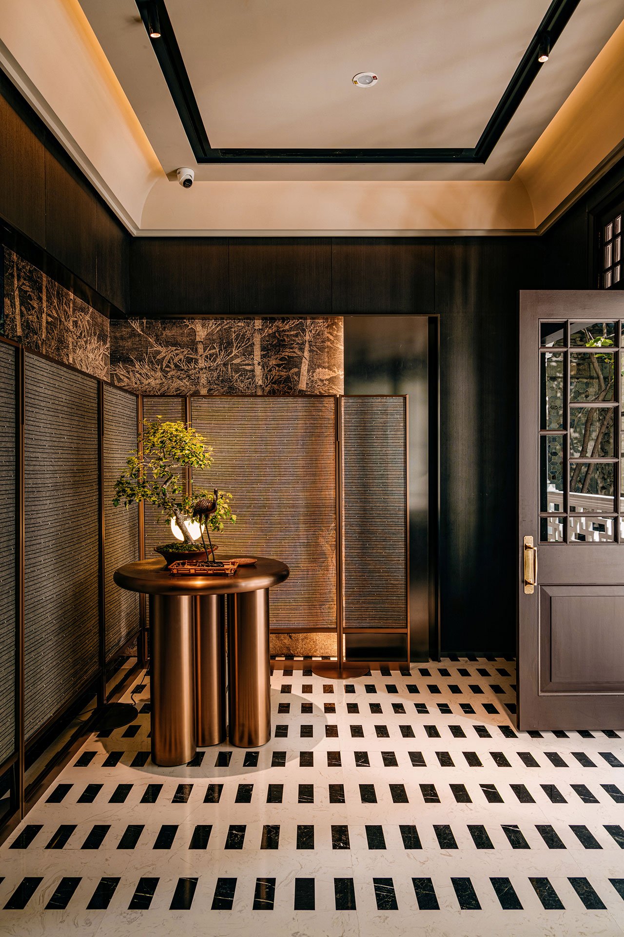 the entry of the restaurant featuring black and white tiles, wood panels and a golden center table