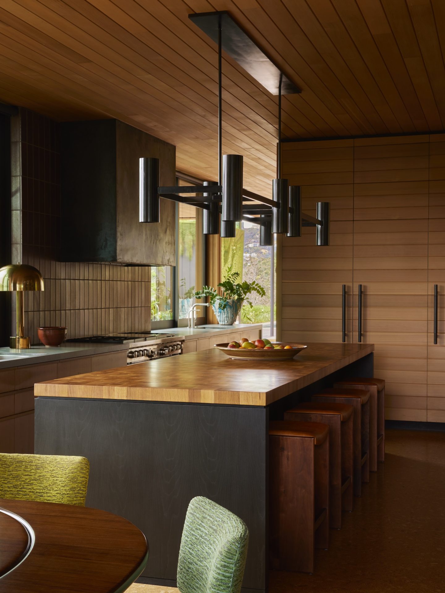 A warm kitchen with wood paneling and a large island. A modern chandelier hangs above, blending seamlessly with the 70s interior design vibe.