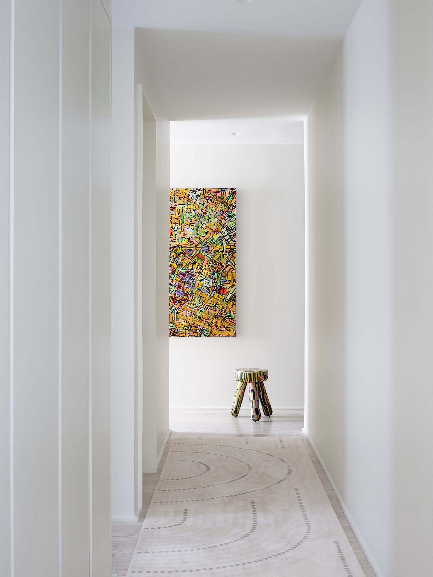 An entry and hall featuring a multicolored abstract painting and matching stool