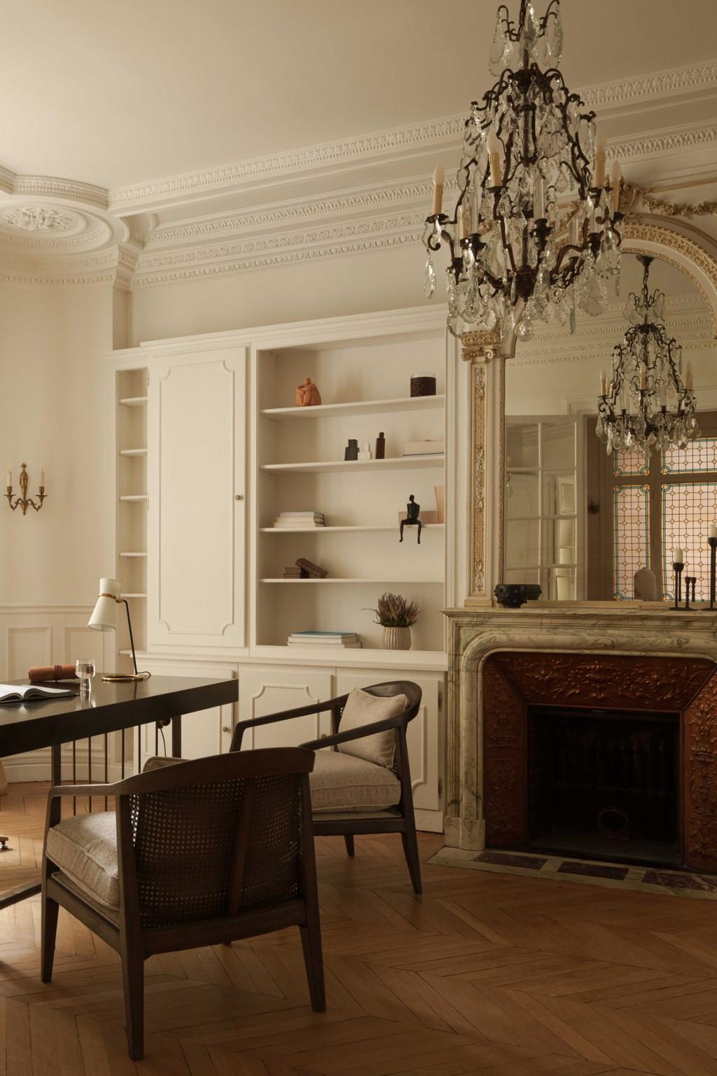 An elegant Parisian study space with a functional twist, featuring a dark wood desk, classic cane-back chairs, and a sculpted marble fireplace. The intricate wall paneling and built-in shelves enhance the timeless charm, while soft neutral tones and herringbone flooring reflect true Parisian interior sophistication.