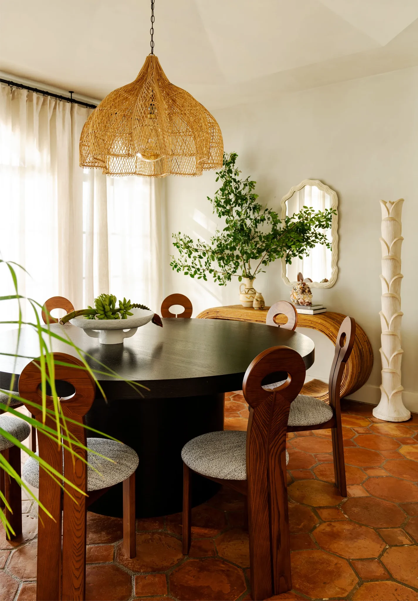 Dining room featuring a circular black wooden table, eight modern sculptured wooden chairs and a rattan chandelier