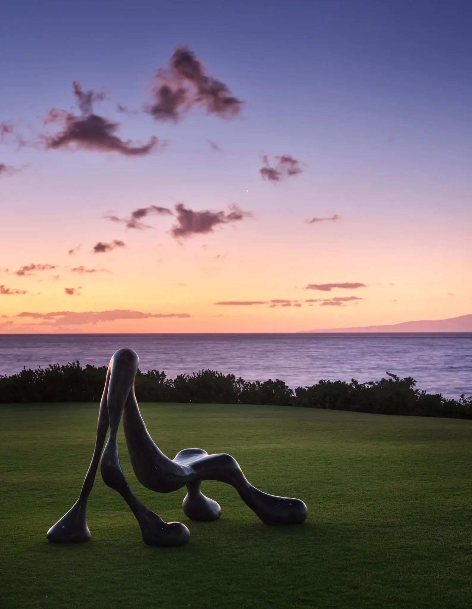 Sculpture garden overlooking a vibrant Maui sunset, blending art with nature in a tropical retreat.