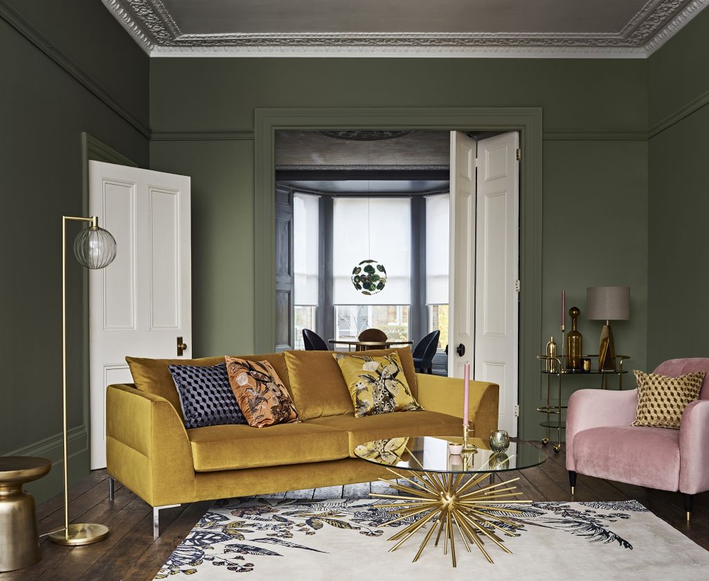 Living room with green walls, a yellow sofa, and a pink armchair that mix vintage and modern furniture