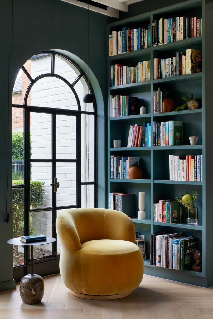 art deco interior design - library room with a bold yellow armchair and a green bookcase 