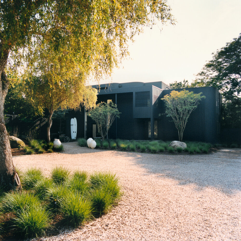 View from the outside of a stunning residence designed by Nate Berkus & Jeremiah Brent. The photo shows a black facade and a green area. 