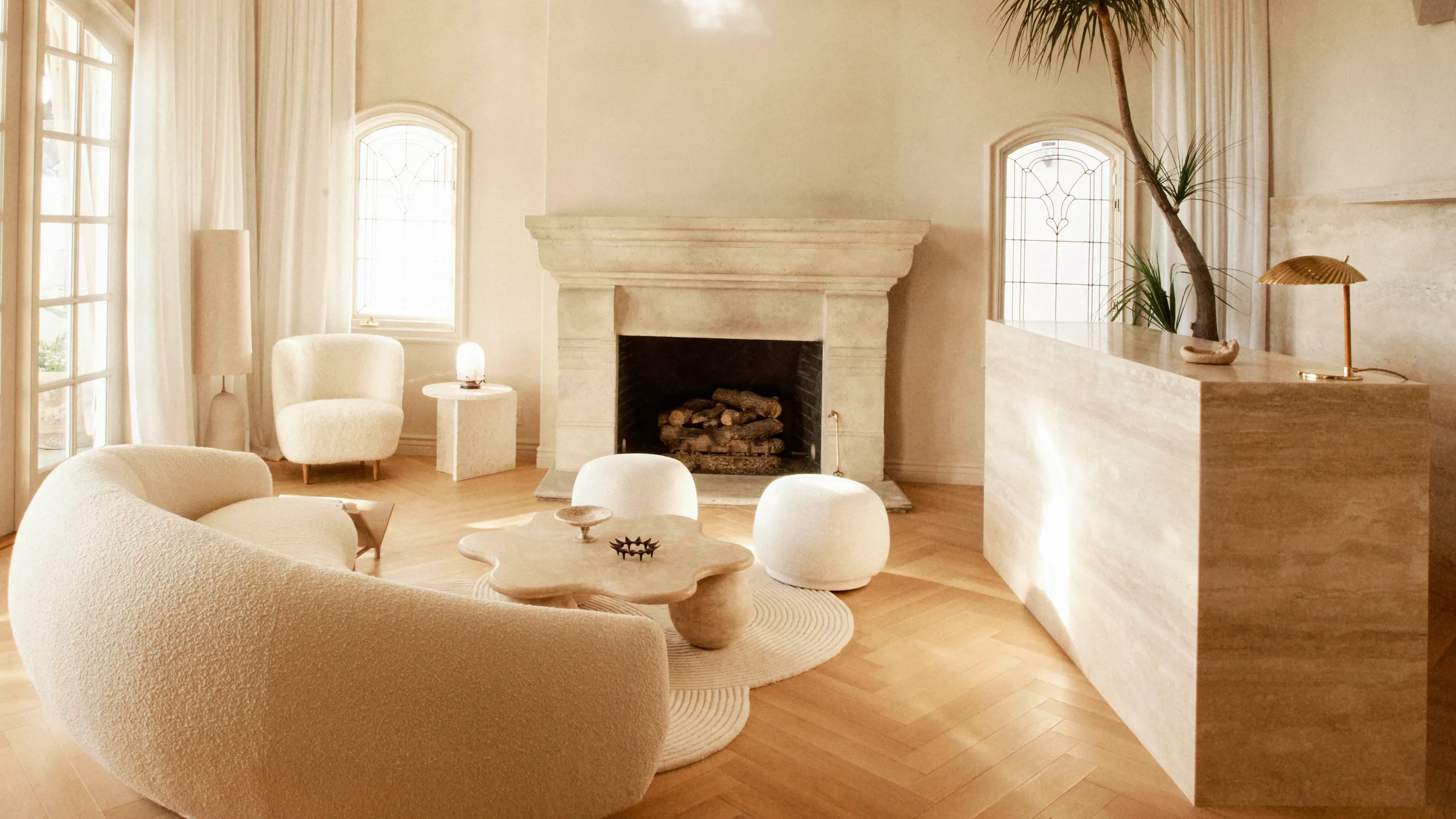 scandinavian design living room with cream walls and with oak wood floors and with a large cream sofa and with a fireplace and with a cream armchair and poufs and stone center table