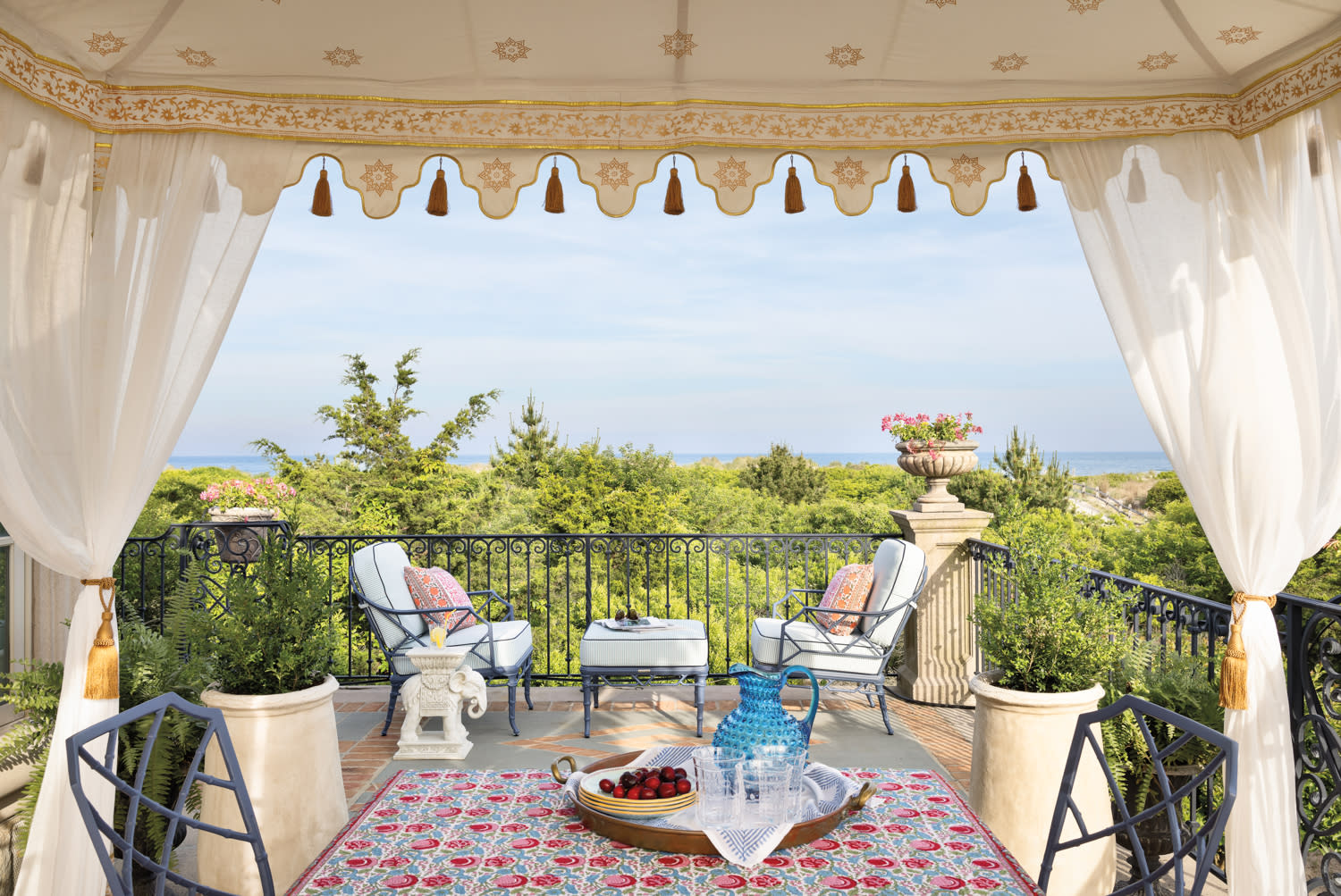 Outdoor terrace with elegant white drapes, patterned rug, and classic lounge seating overlooking a scenic garden view.
