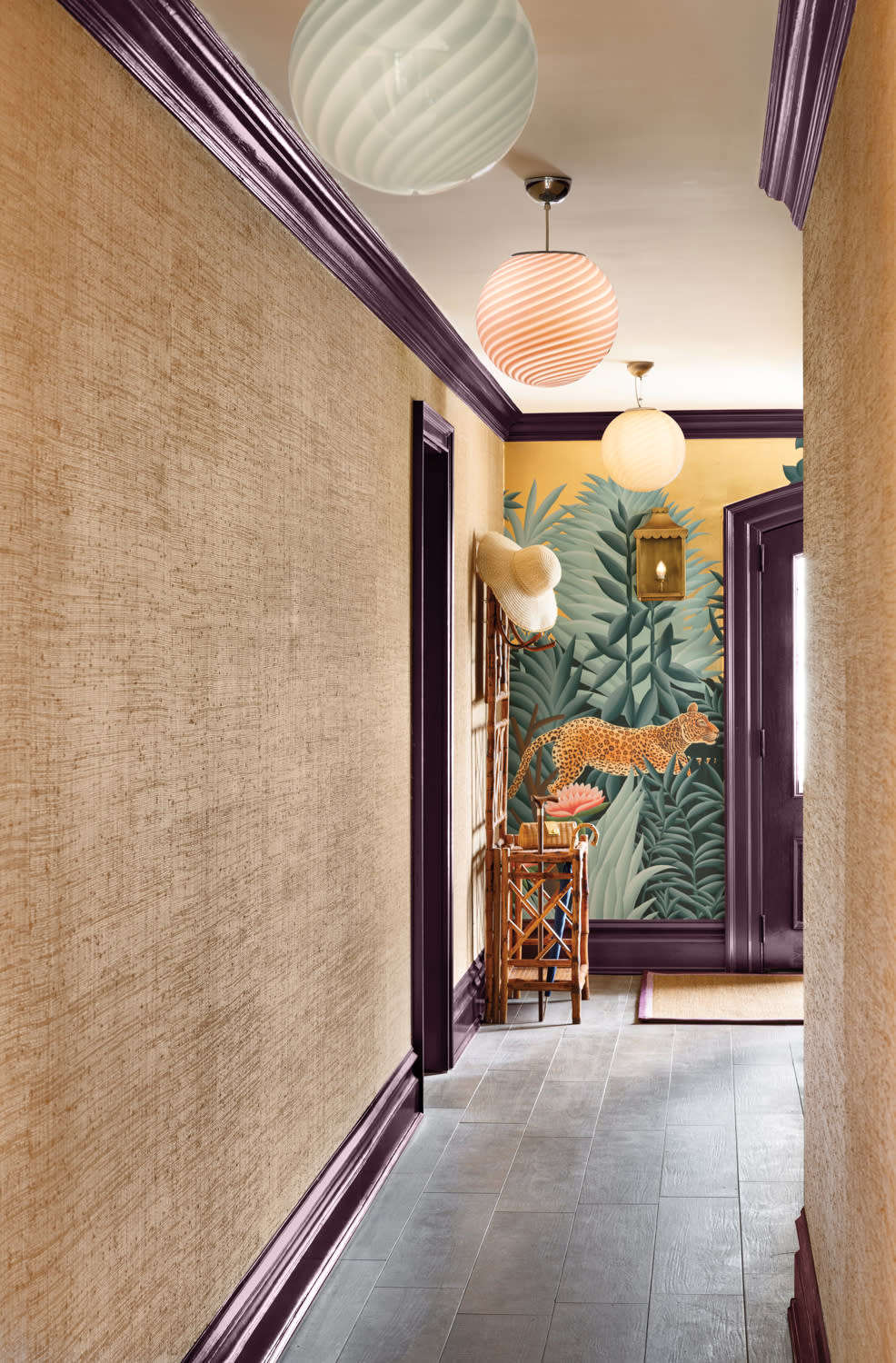 Eclectic hallway featuring a dramatic jungle mural with a leaping leopard, deep plum trim, and natural textured wallpaper. Rattan furniture and paper lantern lighting add warmth and character to the bold entryway.

