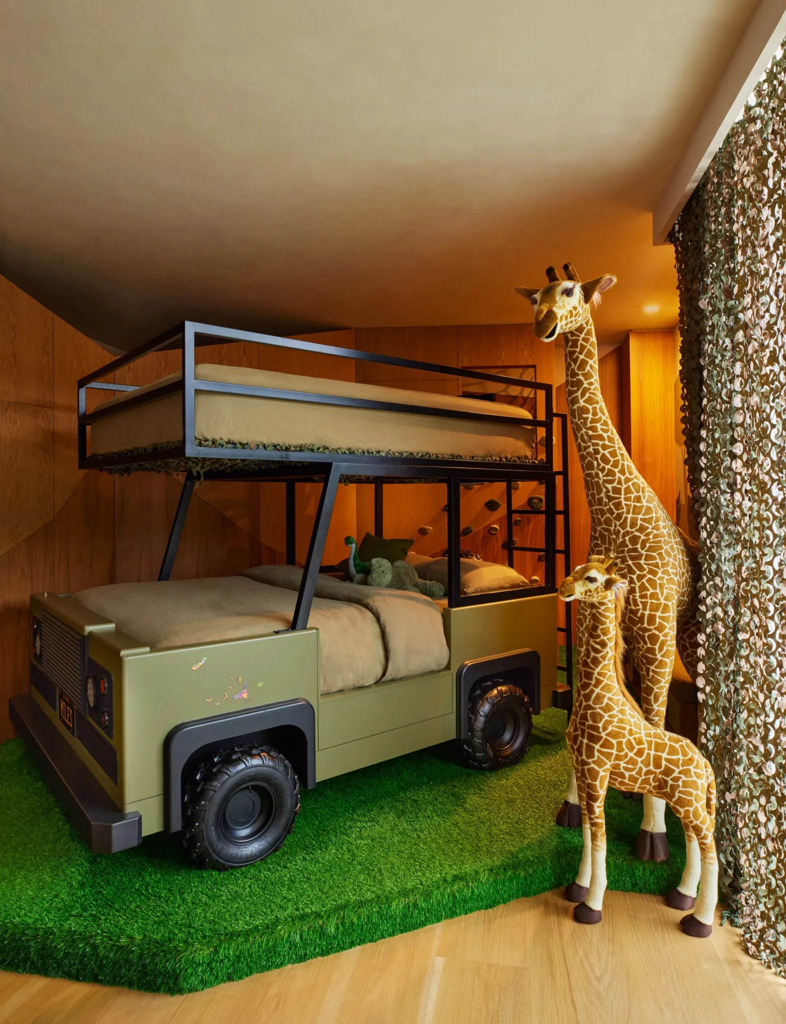 Miles’s bedroom features a custom car bed with operable lights, a climbing wall, and curtains of camouflage netting