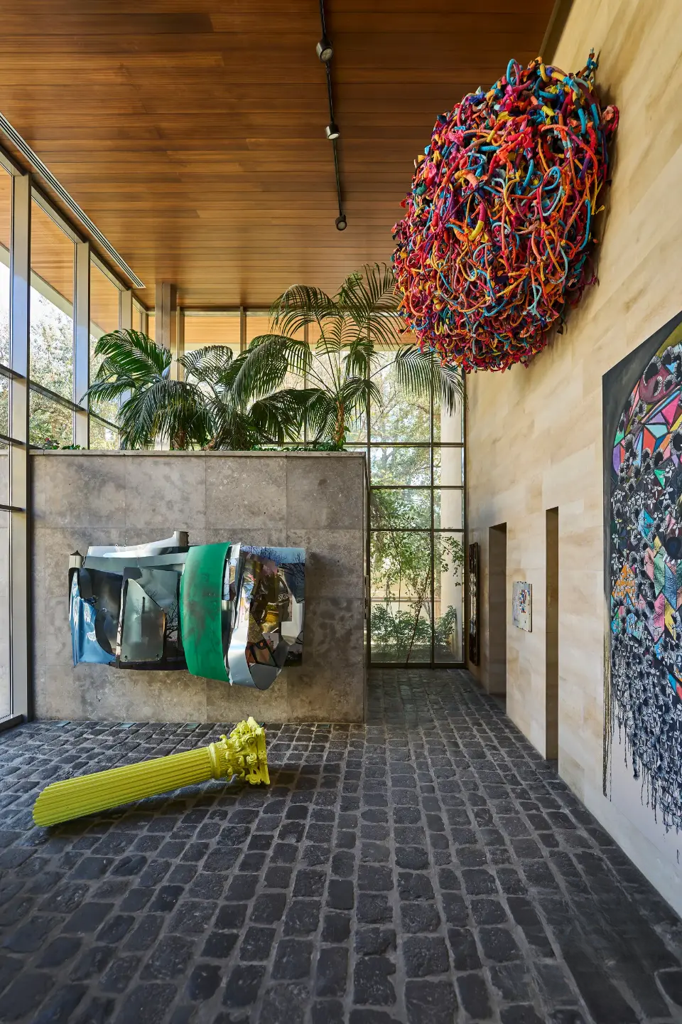 Unique design of a modern villa in Amman featuring bright-colored art pieces on the walls and entry area, large panoramic windows with natural light, cobblestone flooring, and a natural wooden ceiling.