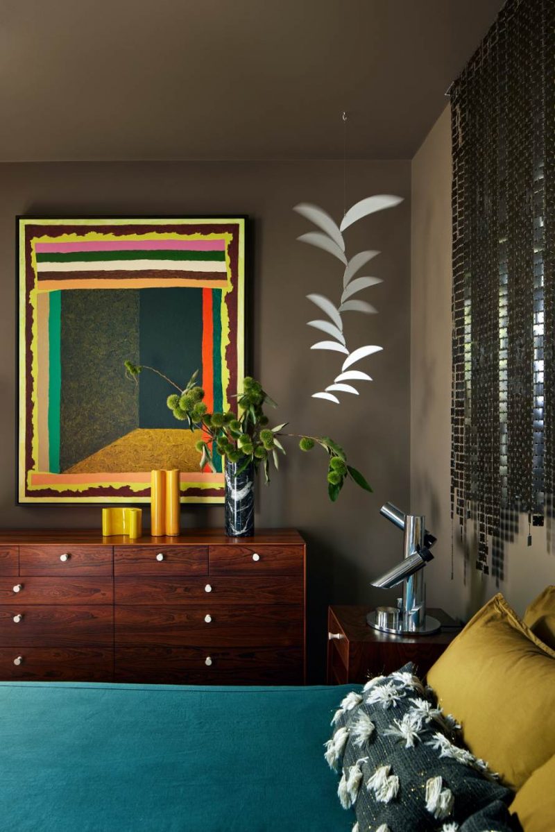 A dark colorful bedroom featuring an abstract painting in vivid colors