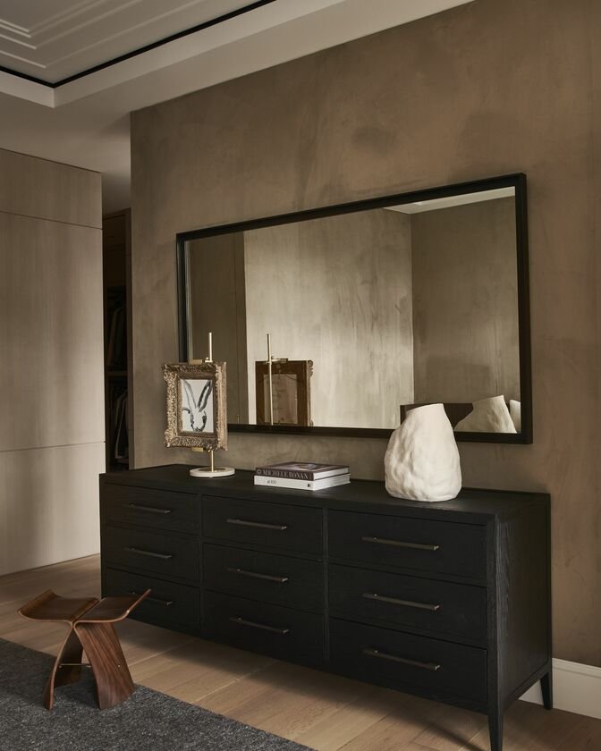 classic chest of drawers and rectangular mirror against an upholstered brown wall in the bedroom