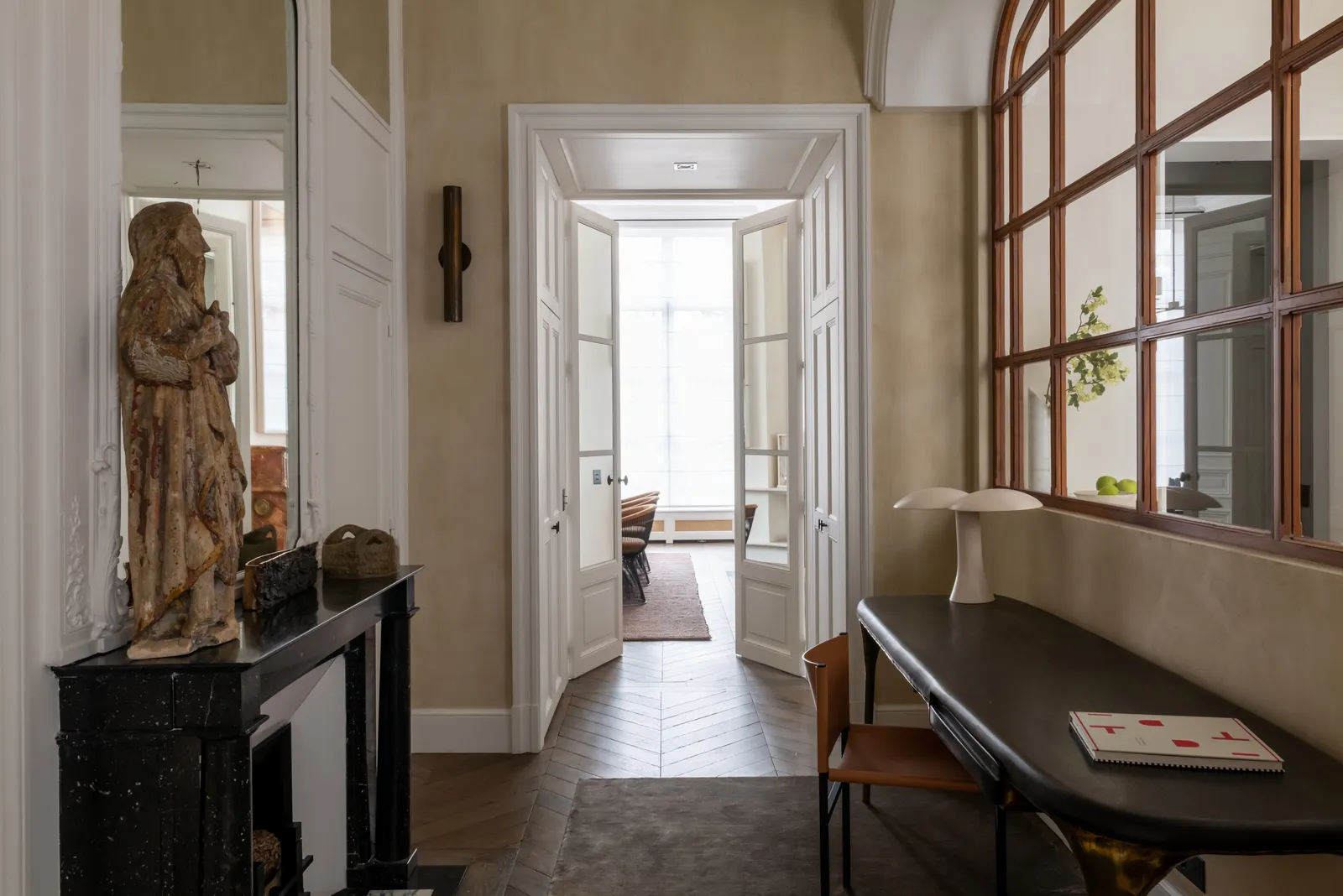 Entrance to Paris apartment featuring wall mirrors for an expanded space effect, a working space crafted from natural wood, and plenty of natural light throughout