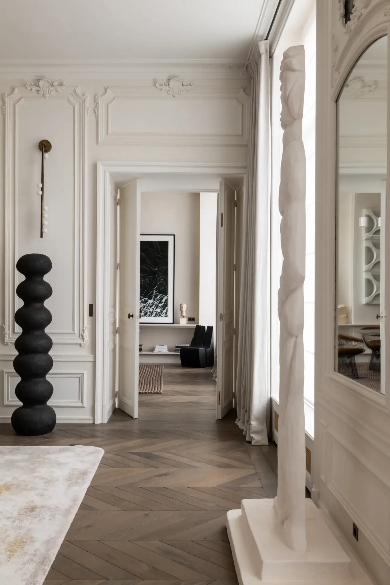 Bright and light-colored living room with wooden parquet flooring, artwork on the walls, whitish wooden doors, and a Limited Edition rug.