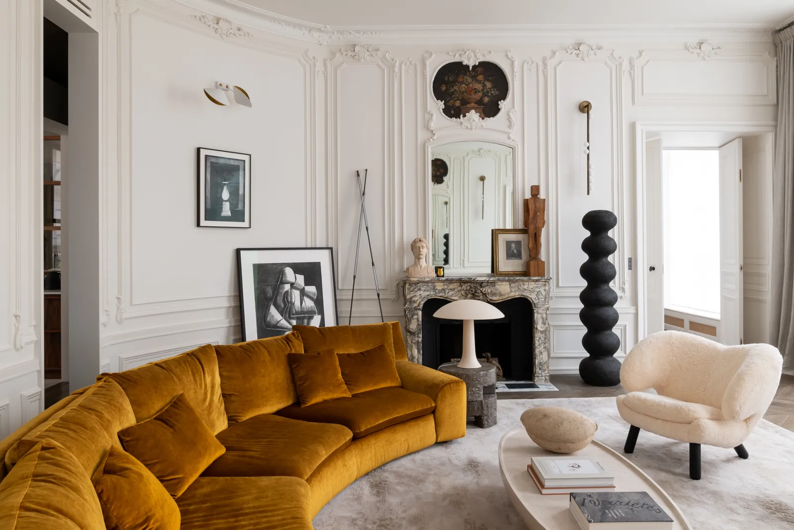 Semi-round sofa and artesanal armchair in a bright Paris apartment living room, featuring exclusive rug, natural light, and curated art work