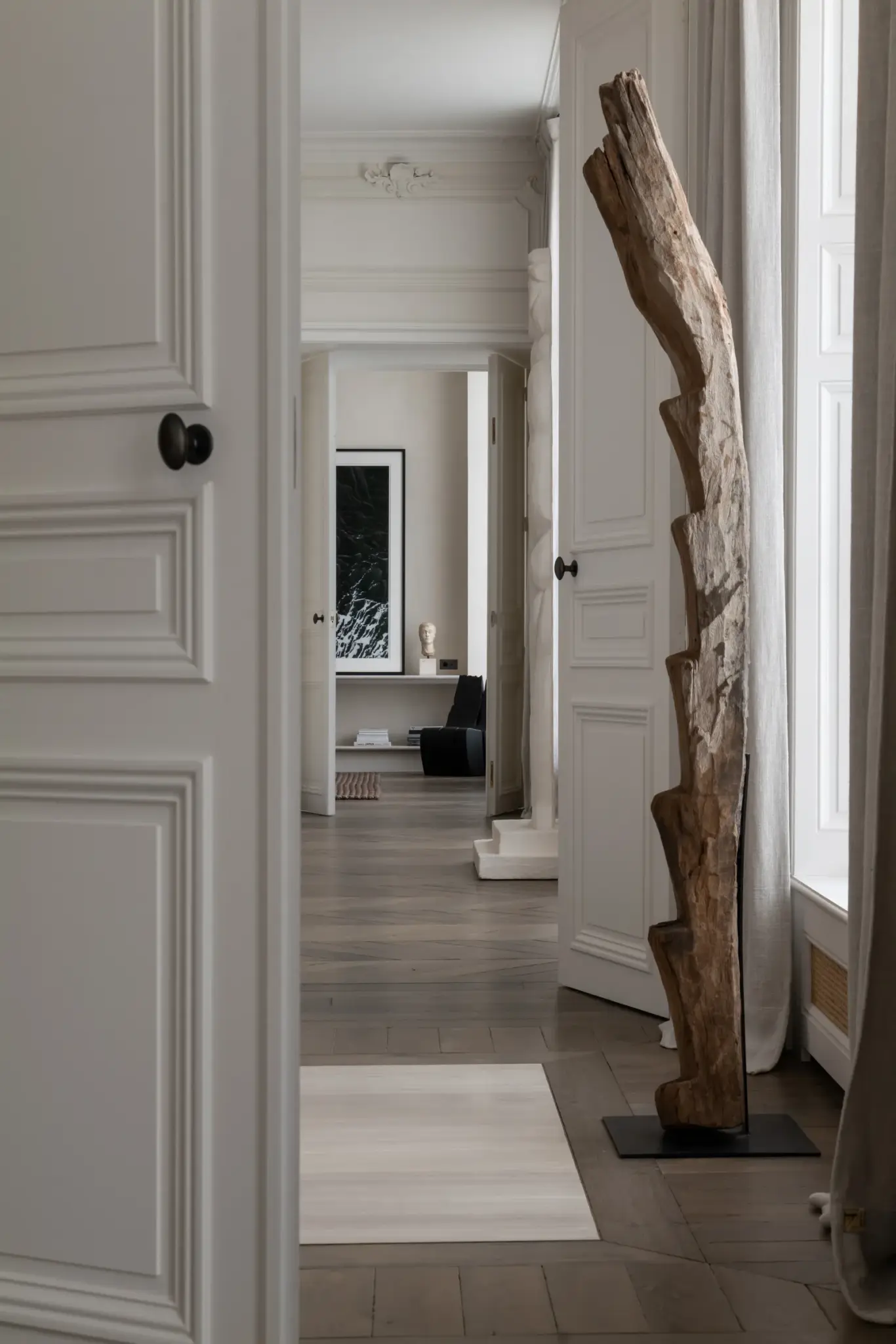 Entrance to Paris apartment with wooden artwork, large windows flooding the space with natural light, and interiors styled in neutral colors and tones