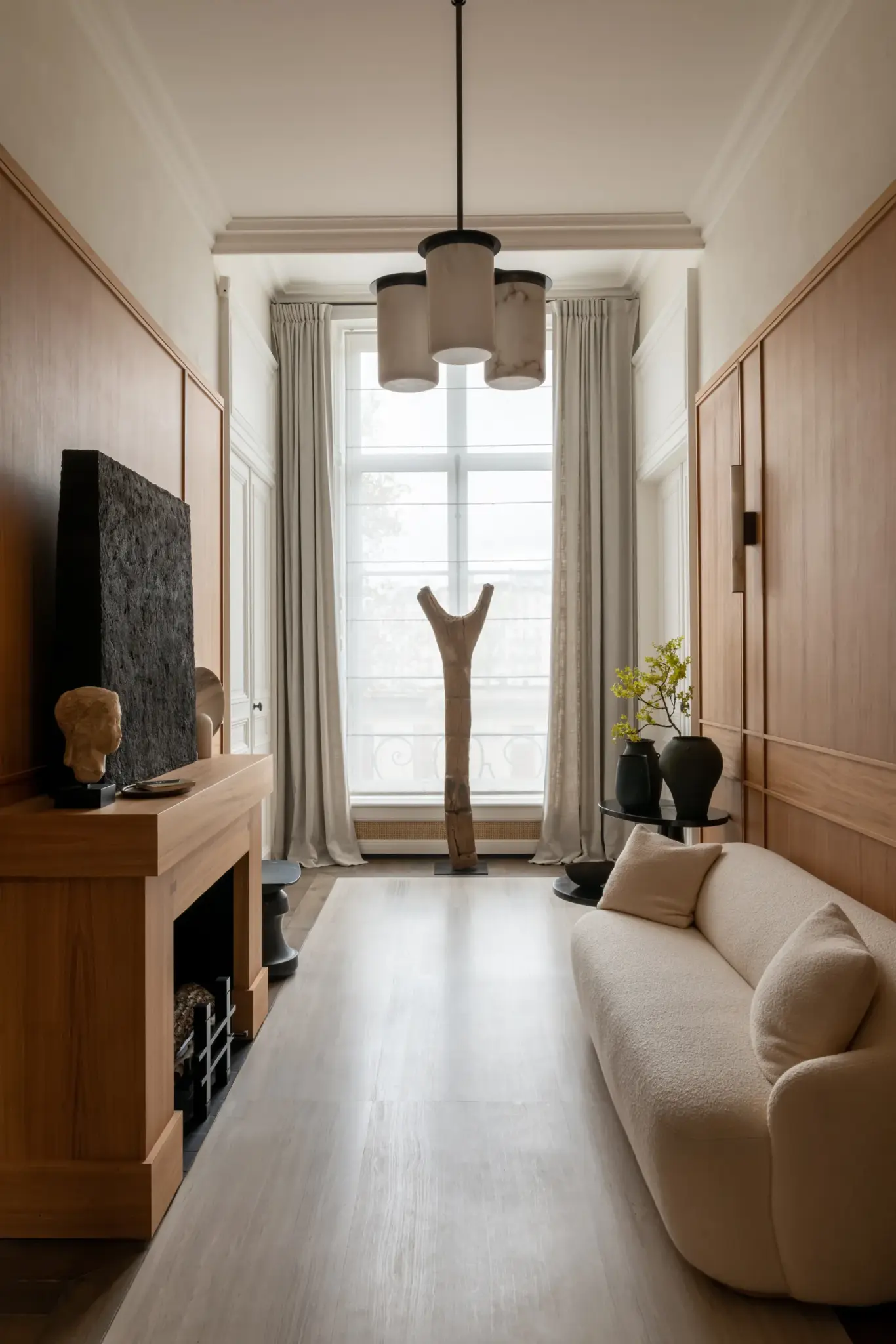 Entrance to the apartment featuring a bright-colored sofa, a huge window letting in natural light, artwork adorning the walls, and a tall wooden sculpture next to the window.