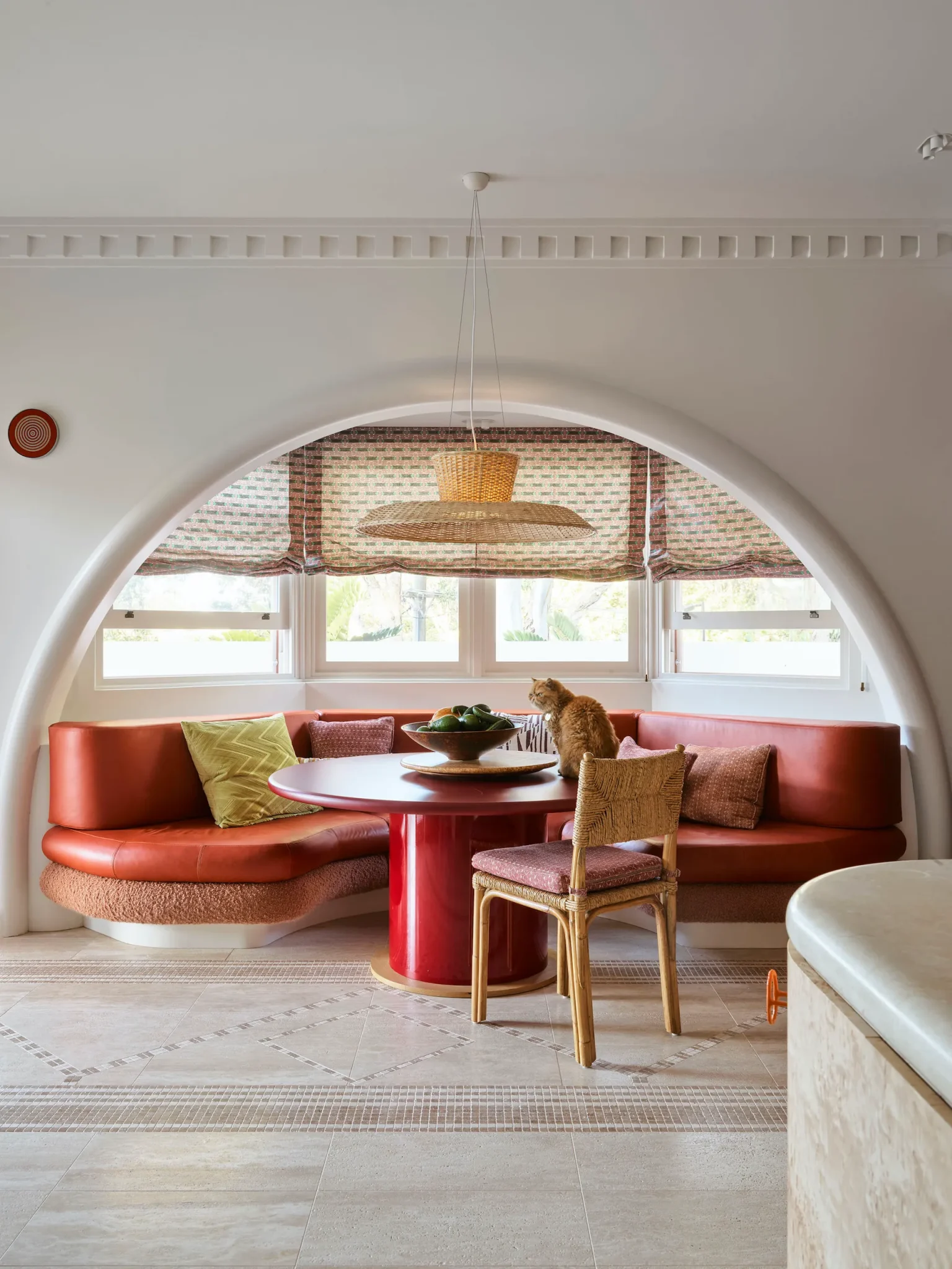 Small dining area on the kitchen featuring a curved red sofa and a round dining table by its center