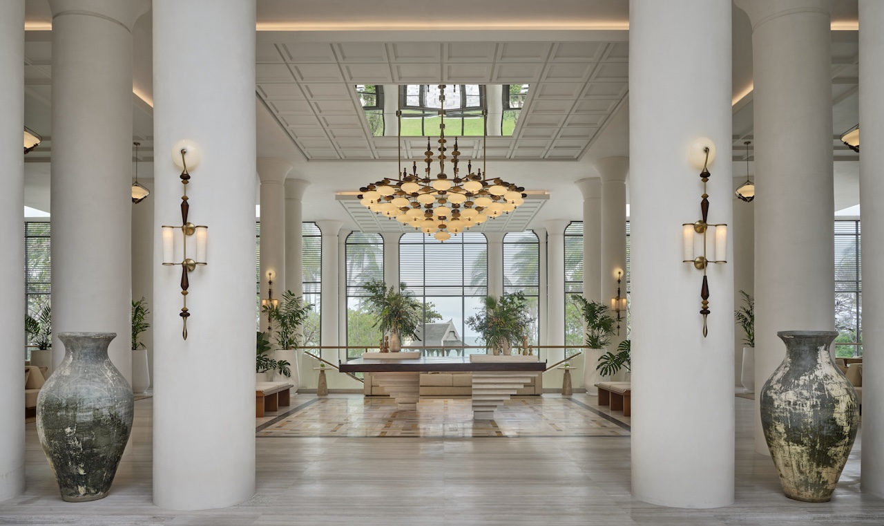 Bright lobby with white columns, a chandelier, and wooden accents.