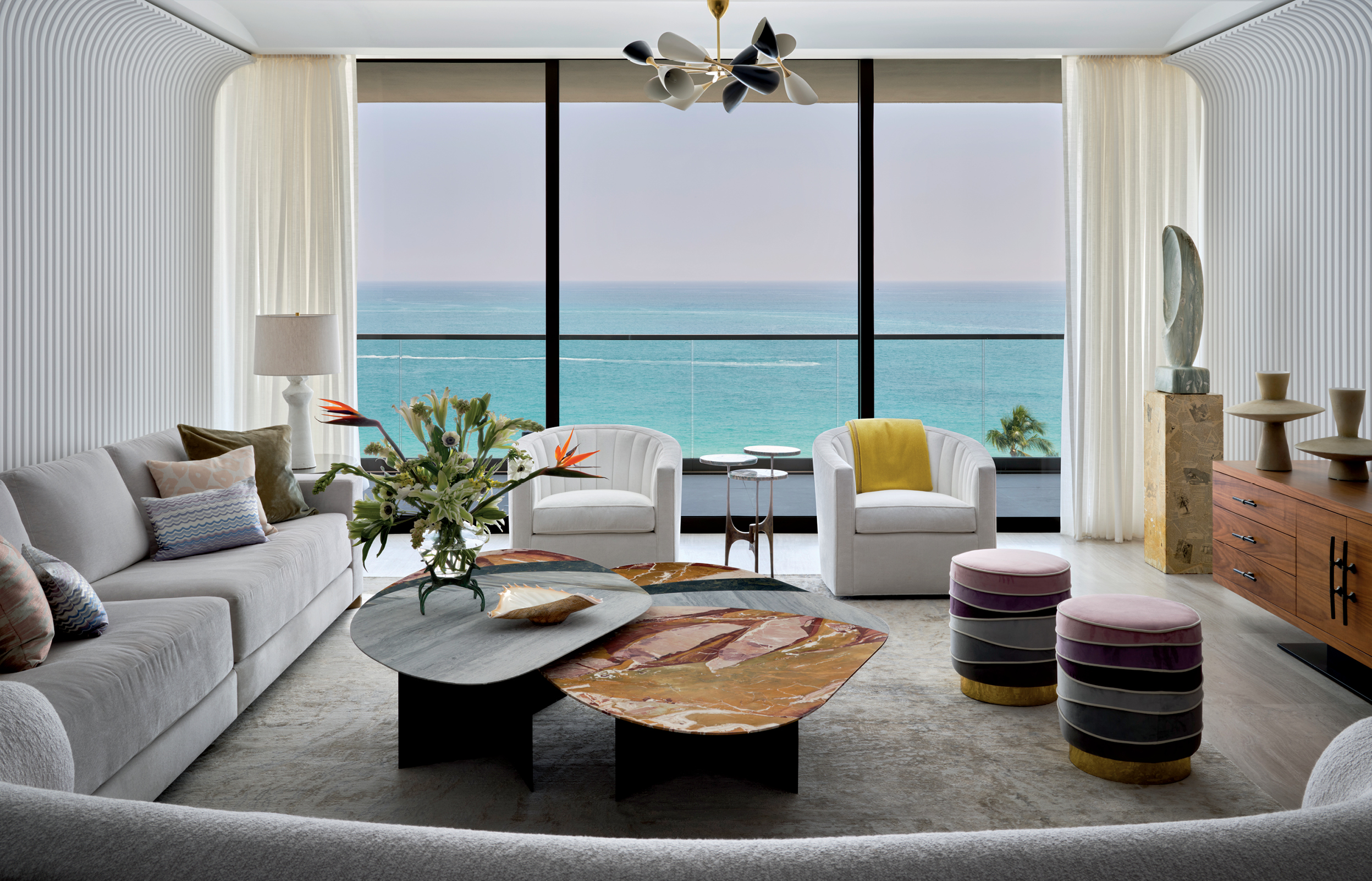 This image depicts a modern Miami living room with a stunning ocean view, featuring curved sofas, unique coffee tables, and contemporary decor. The keyword is "modern miami".
