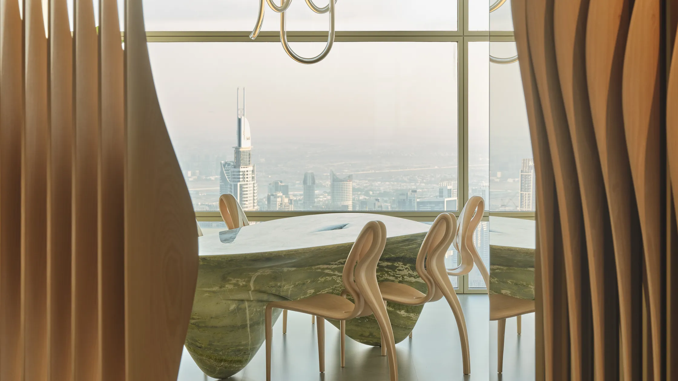 Opulent dining room with city view in Dubai. Marble table, sleek chairs, and modern art under a unique chandelier. Glimpse of houses in Dubai through the window.