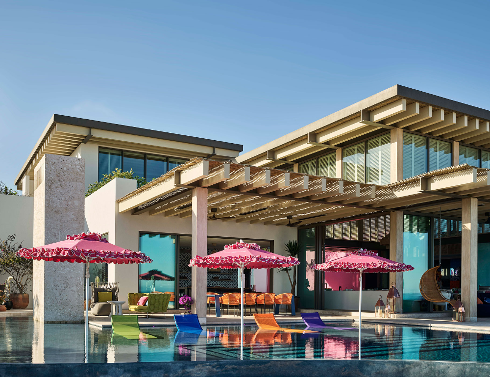outdoor pool featuring 3 pink parasols and 4 multicolored loungers