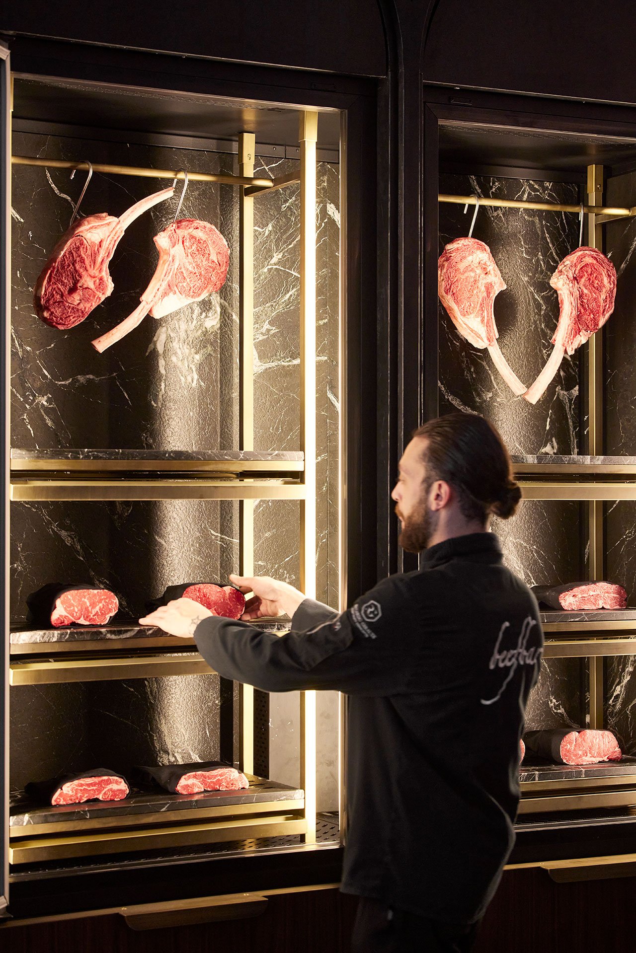 A chef choosing a piece of meat from a restaurant meat displayer