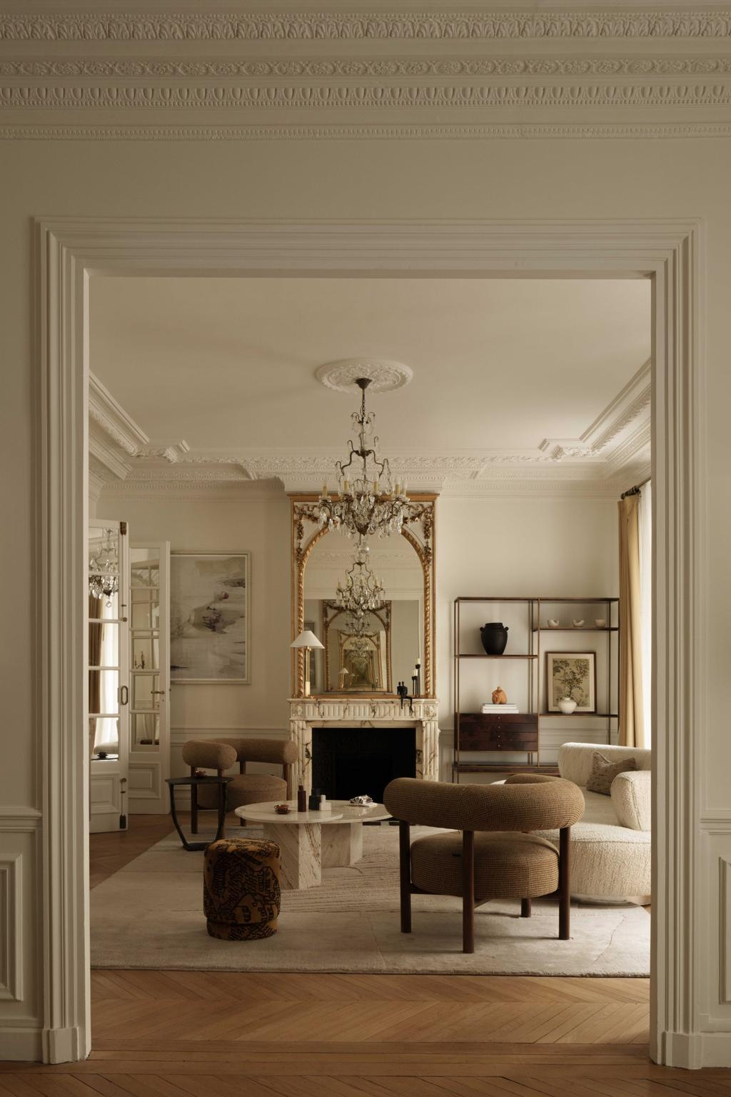 Elegant Parisian salon with fireplace, chandelier, and armchairs viewed through double doors.