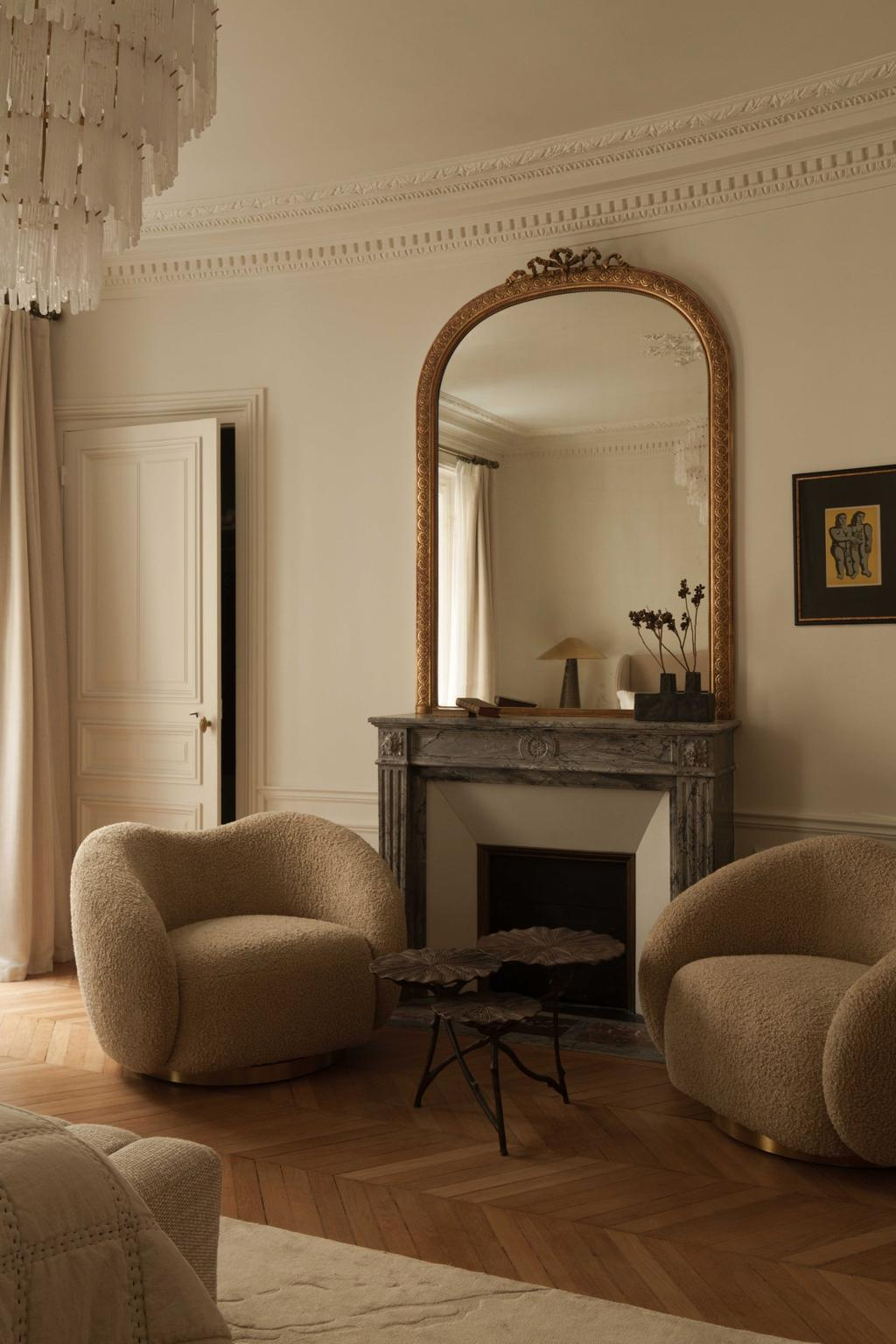 Curved armchair and dark stone fireplace with mirror in a minimalist Parisian interior.