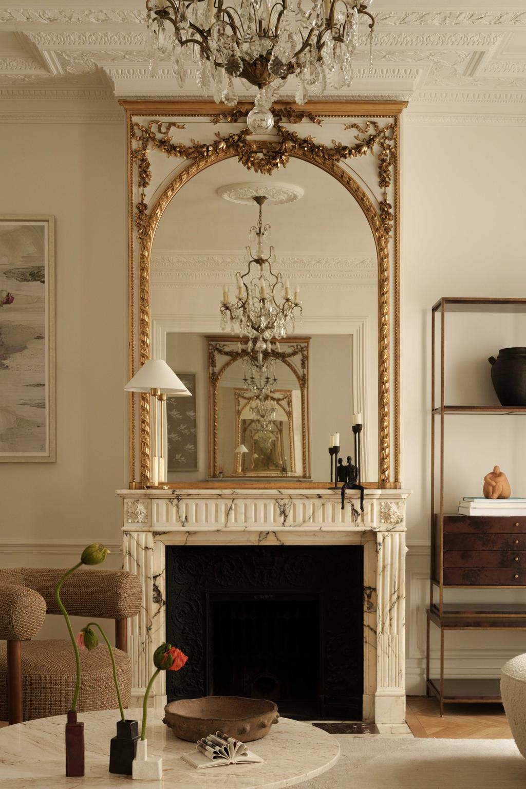 White marble fireplace with antique gold mirror and modern decor in a Parisian apartment living room.
