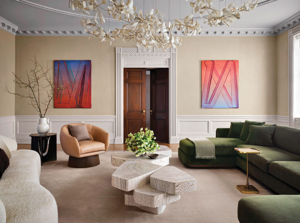 Luxury Interior Design,  A moss-green velvet sofa anchors the space, paired with a cream curved sofa for soft contrast. Between them, stacked pale-wood coffee tables create sculptural interest.