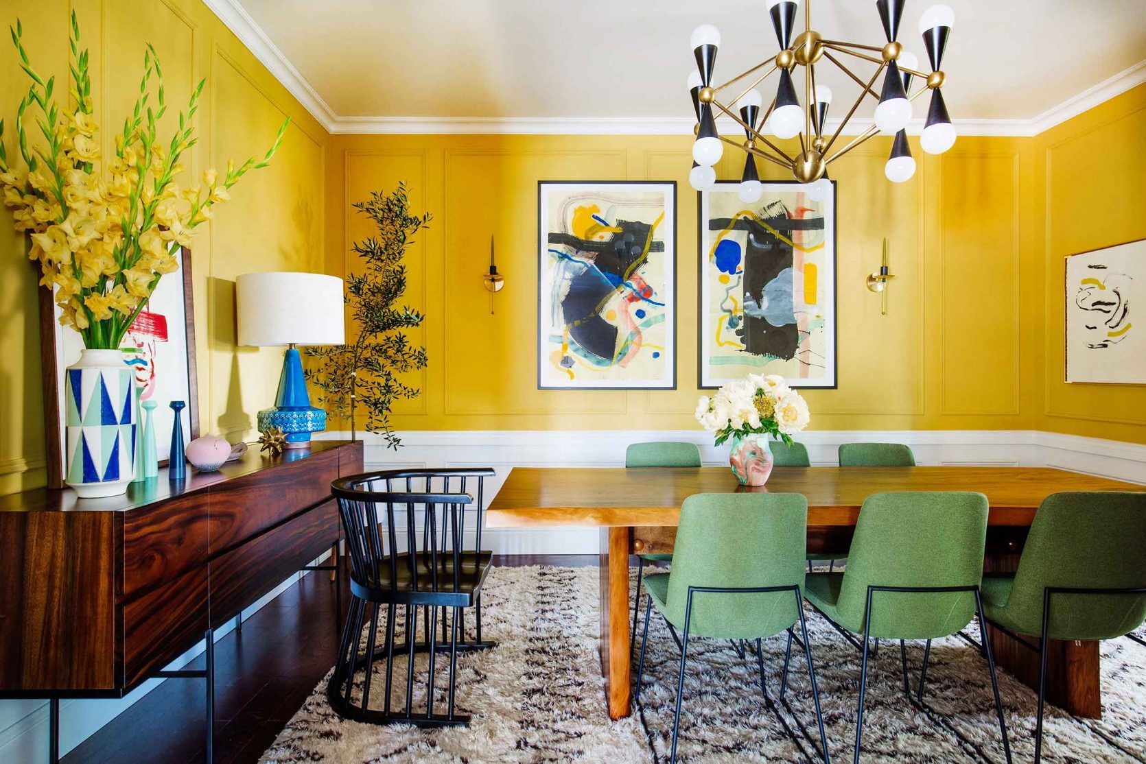 Yellow maximalism styled dining room with wood pieces and green chairs