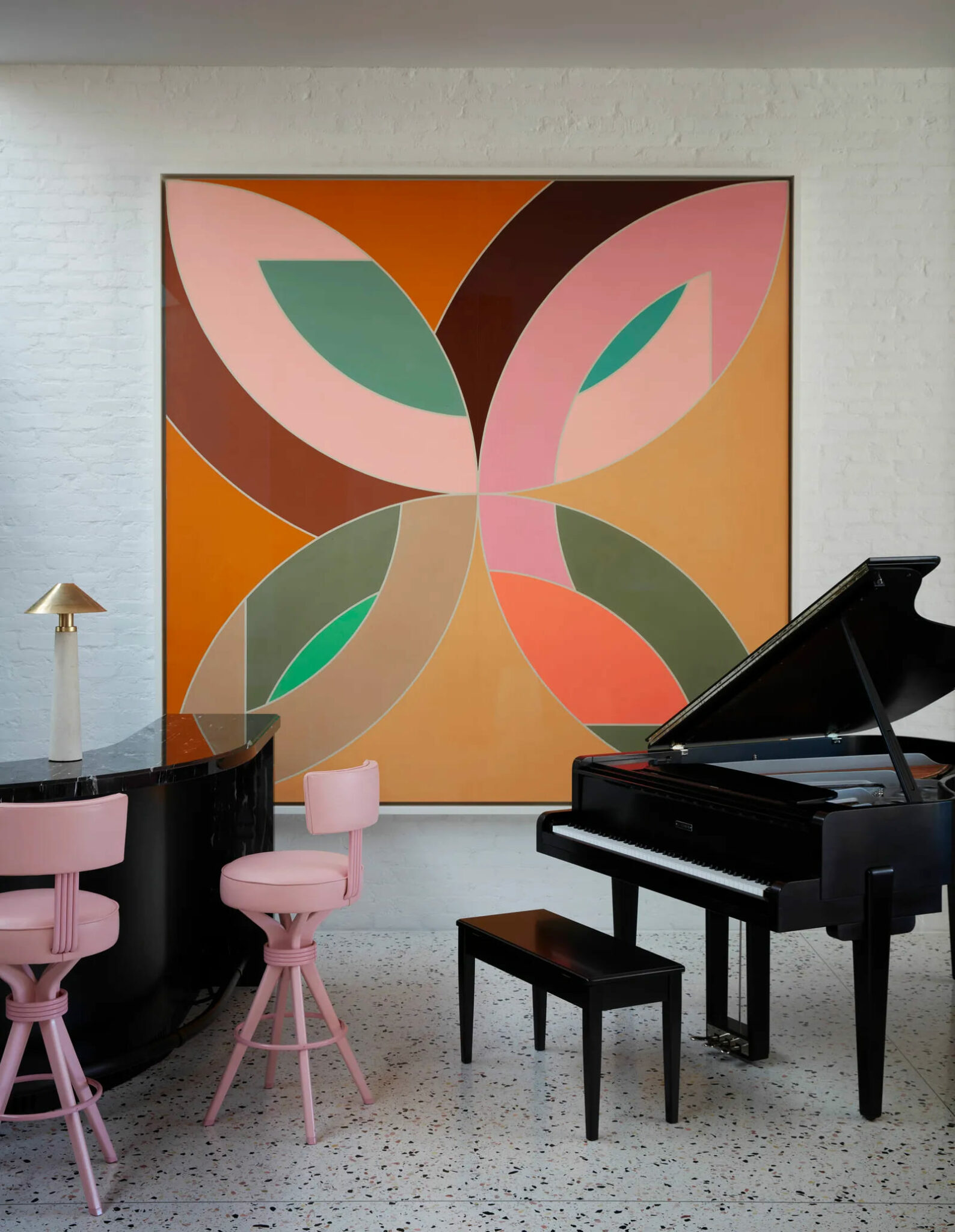 A grand piano next to a colorful painting and a bar with pink bar chairs