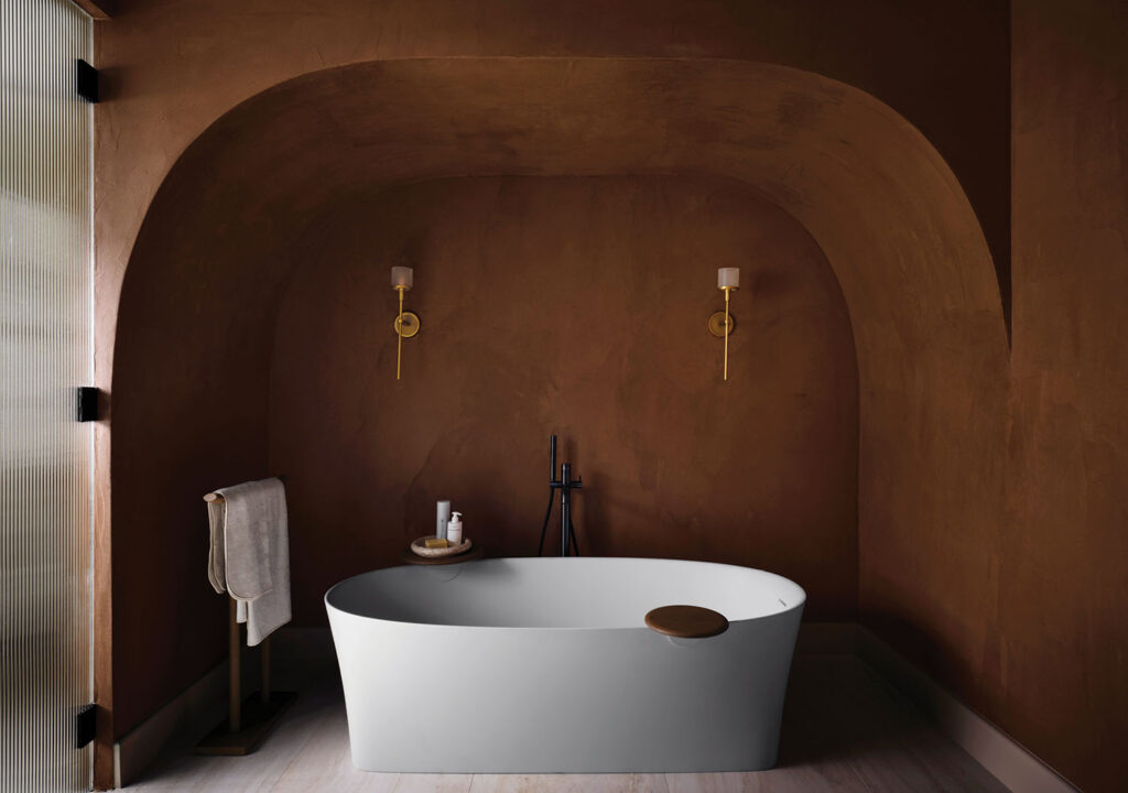 This ensuite bath is a study of sculptural restraint. An earthen plaster alcove frames a sleek freestanding tub, while brass sconces cast a soft, ambient glow. 