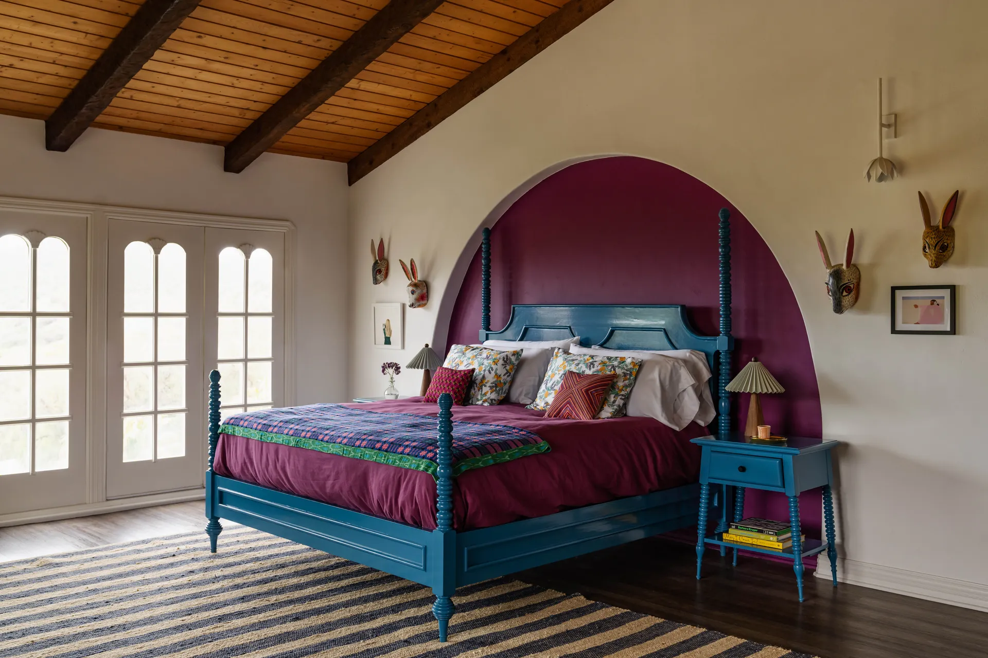 primary bedroom with a electric blue wooden bed set against an arched plum recess