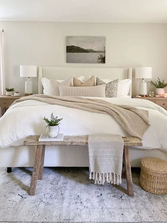A cozy white bedroom with a bed, bench, and rug